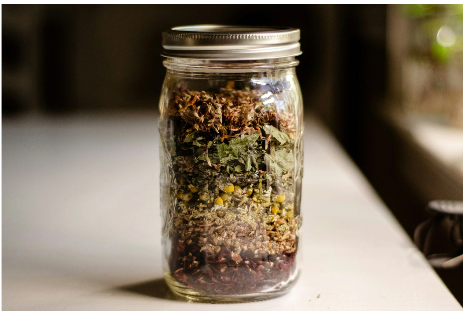 A glass jar layered with dried botanical leaves and flowers